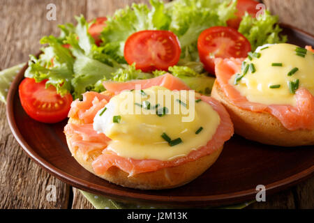 Spiegeleiern mit geräuchertem Lachs, Sauce Hollandaise und frischem Gemüse Nahaufnahme auf einer Platte. horizontale Stockfoto