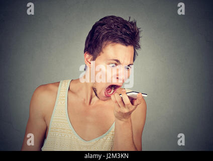 Porträt zorniger junger Mann schreien am Handy auf grauem Hintergrund isoliert. Negative Emotionen Gefühle Stockfoto