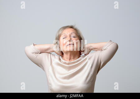 Ältere grauhaarige Frau Hals mit beiden Händen zu berühren, als ob Chondrosis Schmerzen, stehend über einfachen grauen Hintergrund leiden Stockfoto