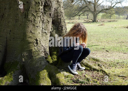 11 Jahre altes Mädchen sitzen unter Baum Stockfoto