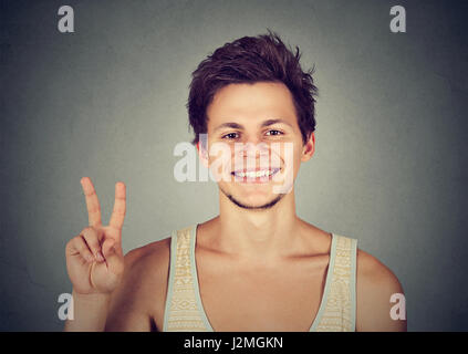 Junger Mann, gut aussehend Student hält Frieden Sieg, zwei Zeichen isoliert grau hinterlegt. Positive menschliche Emotion Gesichtsausdruck Symbole Haltung. Li Stockfoto