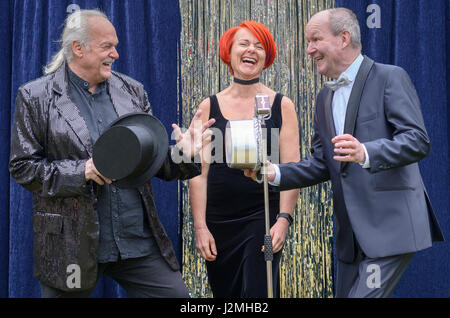 Drei lebhafte Darsteller auf der Bühne feiern vor ein Mikrofon mit einer temperamentvollen rothaarigen Frau und zwei Herren mit Top-Hats, lachen und joki Stockfoto