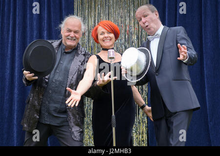Drei lebhafte Darsteller auf der Bühne feiern vor ein Mikrofon mit einer temperamentvollen rothaarigen Frau und zwei Herren mit Top-Hats, lachen und joki Stockfoto