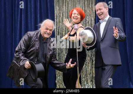 Drei lebhafte Darsteller auf der Bühne feiern vor ein Mikrofon mit einer temperamentvollen rothaarigen Frau und zwei Herren mit Top-Hats, lachen und joki Stockfoto