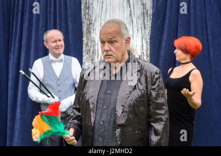 Mann Blick auf bunten Blumen in der Hand ratlos angewidert sah von hinten durch ein Lächeln auf den Lippen Zauberer und seine attraktive Dame Assistentin auf einen Hirsch Stockfoto