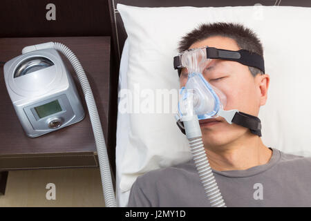 Asiatischer Mann mit Schlafapnoe mit CPAP-Gerät tragen Kopfbedeckungen Maske anschließen, um Luft-Schlauch, selektiven Fokus auf den Mann und Kopfbedeckungen Maske Stockfoto
