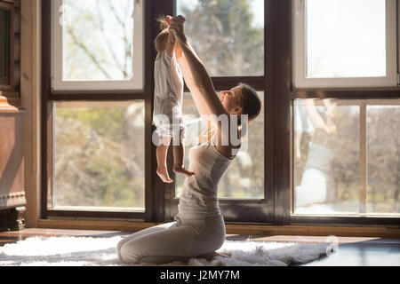 Junge sportliche Mutter Übungen mit ihrem Kind zu Hause arbeiten, zusammen zu spielen, Holding-Tochter in der Luft, wirksame und sichere Training, Praxis Stockfoto