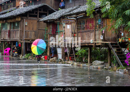 Zhaoxing, Guizhou, China, ein Dong Minderheit Dorf.  Junge Frau mit einem bunten Regenschirm die Straße hinunter. Stockfoto