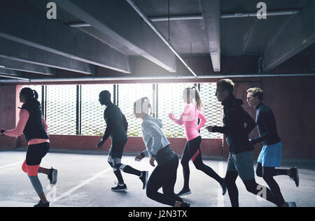 Gruppe von aktiven jungen Freunden urbanen laufen, sprinten wie ein Rudel durch eine kommerzielle Tiefgarage in einem Gesundheits- und Fitness-Konzept Stockfoto