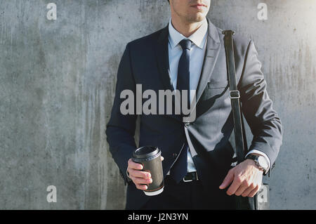 Ein Geschäftsmann, eleganten Anzug mit dem Kaffee Tasse Stand in der Nähe der grauen Wand. Stockfoto