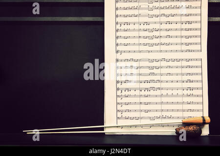 Notenblätter und des Dirigenten Schlagstöcken auf schwarzem Metall stehen im warmen Retro-Farbton, mit Platz für Textfreiraum Stockfoto