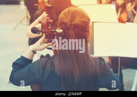 Blick auf die Rückseite des eine asiatische Frau Cello-Spieler in ein kostenloses Konzert im Freien in einem öffentlichen Park, während des Sonnenuntergangs mit leichten Flare-Effekt und Vintage Farbe st Stockfoto