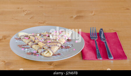 Crêpe mit Schokolade und Schokolade-Chips und Schokolade Topping auf weißen Teller auf einem Holztisch mit Gabel und Messer auf einer roten Serviette serviert Stockfoto