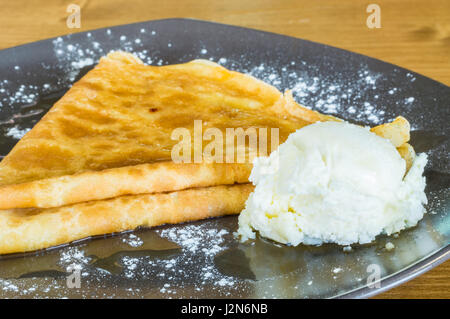 Nahaufnahme von leckeren Crêpe mit Honig und Eis serviert auf einer grauen Platte auf einem Holztisch Stockfoto