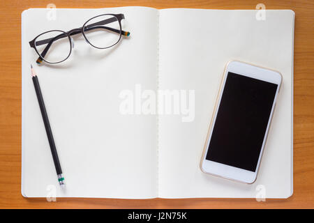 Brillen, Bleistift und Handy, auf offenen weißen Notizbuch auf Holztisch Stockfoto