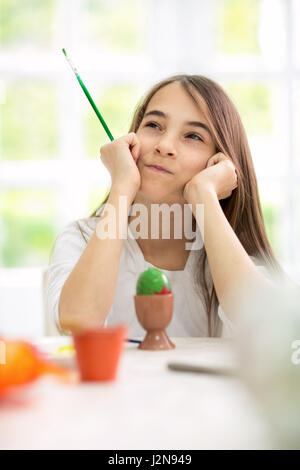 schöne Mädchen denken, auf der Suche nach Ideen für das Bemalen von Ostereiern Stockfoto