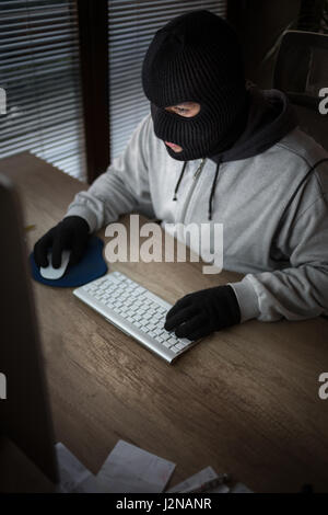 maskierte Dieb mit Sturmhaube sitzen vor dem computer Stockfoto