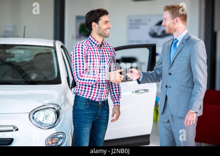 Absatzsituation in einem Autohaus, die Händler geben der Auto-Taste bei jungen männlichen Stockfoto