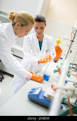 Zwei junge Techniker im chemischen Labor legen Flüssigkeit mit Lab pipette Stockfoto