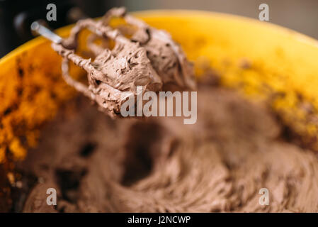 Teig und Schokoladenpulver Schlagsahne in Schüssel mit einem Mixer-Detailansicht. Süße Kuchen Zutaten Zubereitung Stockfoto