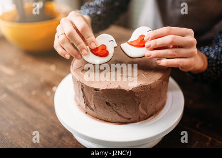 Weibliche Hände verzieren Kuchen mit Keksen in Form von Vögel. Hausmannskost, leckere Nachspeise Stockfoto