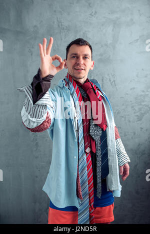 Lächelnd Mann in viele Kleider gekleidet zeigt OK Zeichen. -Shopping-Konzept Stockfoto