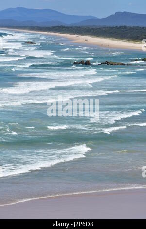 Sandstrand mit weißen ozeanischen Surf südlich von Tacking Point Lighthouse in Port Macquarie mit drei Brüdern in weit im Hintergrund. Stockfoto