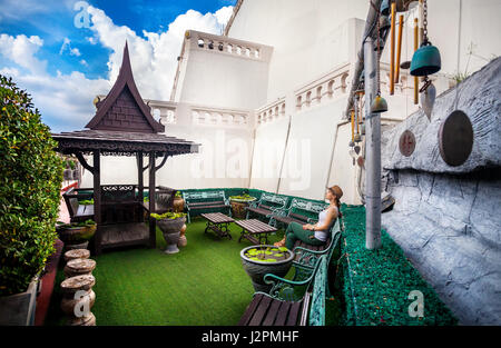 Frau Tourist in Hut sitzt auf der Bank im Garten am Wat Saket, auch bekannt als Golden Mount in Bangkok, Thailand Stockfoto