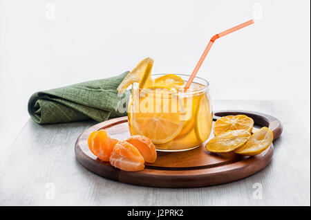 Orange kaltes Getränk mit Eis, Limonade mit Scheiben von Orange und Mandarine in einer durchsichtigen Schüssel auf einem runden Holzsockel Stockfoto