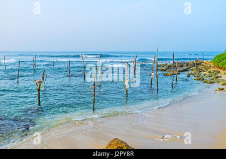 Die hohen Wellen am Strand von Ahangama, voll von Sticks für eine der traditionellen Formen der Fischerei im Indischen Ozean, Sri Lanka. Stockfoto