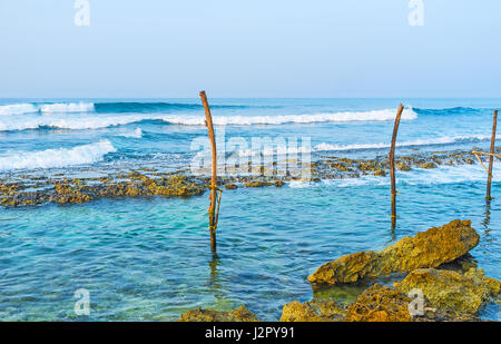 Morgens Wellen am Ahangama Strand mit dem alten Fischerhafen Sticks im Vordergrund, Sri Lanka. Stockfoto