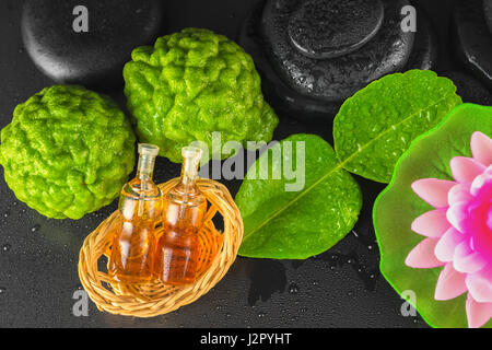 Draufsicht der Spa Konzept Bergamotte, Blatt, Duftöl, Lotus und Zen Basalt Steinen mit Wasser Tau auf schwarzem Hintergrund, Nahaufnahme Stockfoto