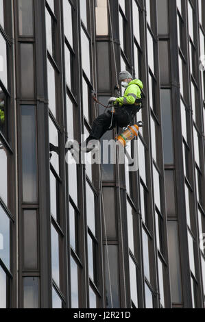 Ein Mann skaliert ein high-Rise Bürohaus in Cardiff, Wales. Sprühen Unkrautvernichtungsmittel Stockfoto