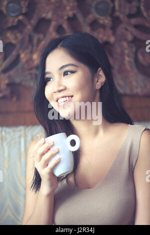 Asiatische Frau hält eine Tasse Kaffee mit Blick hinter der Kamera Stockfoto