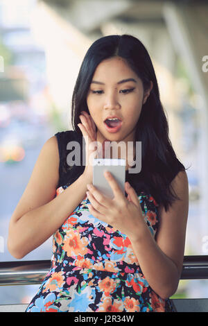 Asiatische Frau sah überrascht auf ihrem Handy Stockfoto