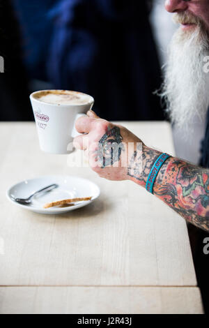 Eine Kaffeetasse in eine tätowierte Hand Tattoos Designs Kaffeepause Erfrischung Kaffee trinken statt Stockfoto