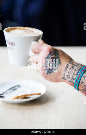 Eine Kaffeetasse in eine tätowierte Hand Tattoos Designs Kaffeepause Erfrischung Kaffee trinken statt Stockfoto