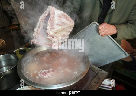 Ein Alter Mann kochen Schweinefleisch auf dem Herd und ein Stück der Rippen. Stockfoto