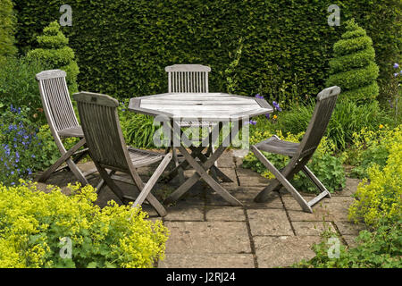 Holztisch mit vier Stühlen auf kleine zerschlug Gartenterrasse mit grünen Grenzen und Formschnitt durch Barnsdale Gärten, Rutland, England, UK Stockfoto