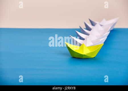 Leuchtend gelbe Papier Schiff führenden weissen basierend auf blau gegen hellen Hintergrund. Handmade und Origami. Reise um die Welt. Reise- und transporta Stockfoto