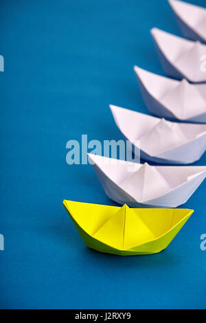 Leuchtend gelbe Papier Schiff führenden weissen basierend auf blau. Handmade und Origami. Reise um die Welt. Reise und Transport. Ocean und das Meer. Conc Stockfoto