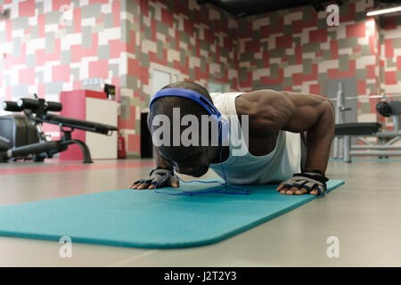 Zuversichtlich bemuskelt junge Mann trägt Sport tragen und tun Planke Position während dem Training auf dem Boden im Fitness-Studio Stockfoto