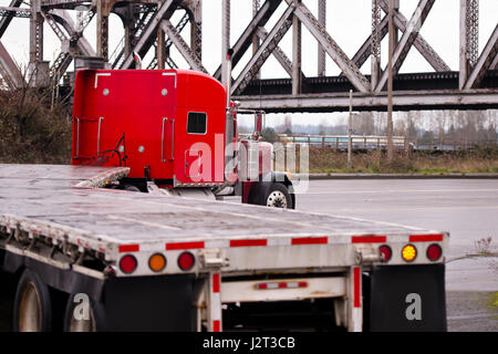 Klassische große mächtige rote Sattelschlepper mit Kapuze in einer Kurve in der Straße mit einem Tieflader mit roten Etiketten restriktive Sicherheit Stockfoto