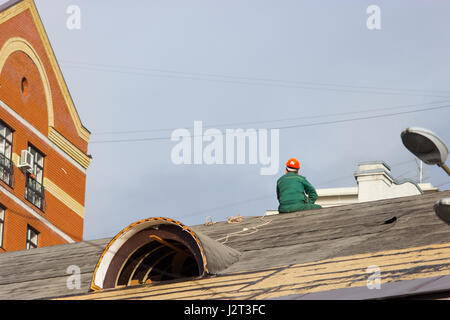 Arbeiter in einen Helm sitzen auf dem Dach des Gebäudes Stockfoto