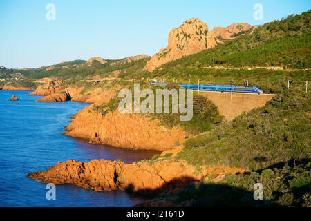 Hochgeschwindigkeitszug auf einer Landschaft aus rotem Vulkangestein (Rhyolith) bei Sonnenaufgang. Estérel Massif, Saint-Raphaël, Var, Provence-Alpes-Côte d'Azur, Frankreich. Stockfoto