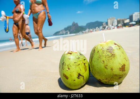 Paar von frischem Grün Kokosnüssen trinken am Ufer ausruhen, während Leute am Strand von Ipanema in Rio De Janeiro, Brasilien vorbeigehen Stockfoto