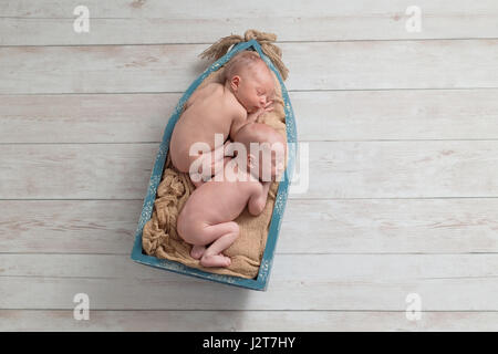 Sechs Tage alten Zwillingsbruder, Neugeborenes, Baby jungen schlafen in einem kleinen, hölzernen Boot. Gedreht im Studio auf einem hölzernen Hintergrund. Stockfoto
