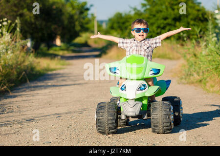 Glückliche kleine Junge spielen unterwegs in der Tageszeit. Er fährt mit Quad im Park. Kind mit Spaß an der Natur. Konzept des Glücks. Stockfoto