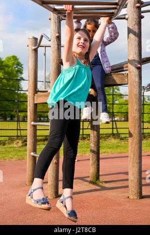 Vertikale Porträt eines jungen Mädchens schwingen entlang Klettergerüst auf einem Spielplatz. Stockfoto