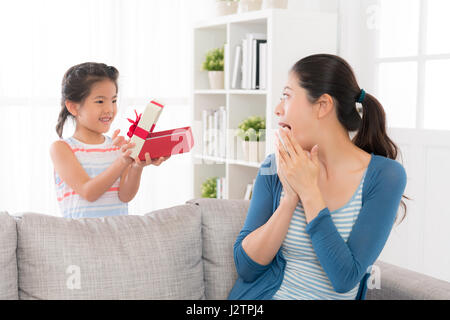 asiatische chinesische Mutter am Tag der Mutter erhielt ein rot Geschenk von der kleinen Tochter Gefühl aufgeregt und zeigt Emotionen sitzen auf dem Sofa in der l Stockfoto